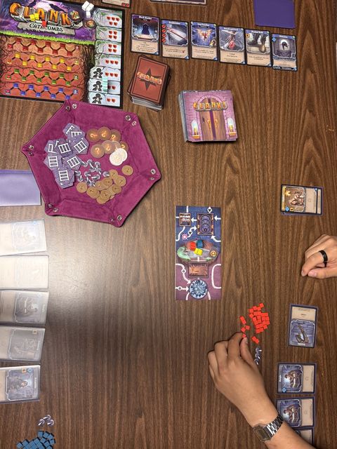 Overhead view of a Clank! Catacombs game in progress, with the mastery track, dungeon deck, and market cards laid out on the table